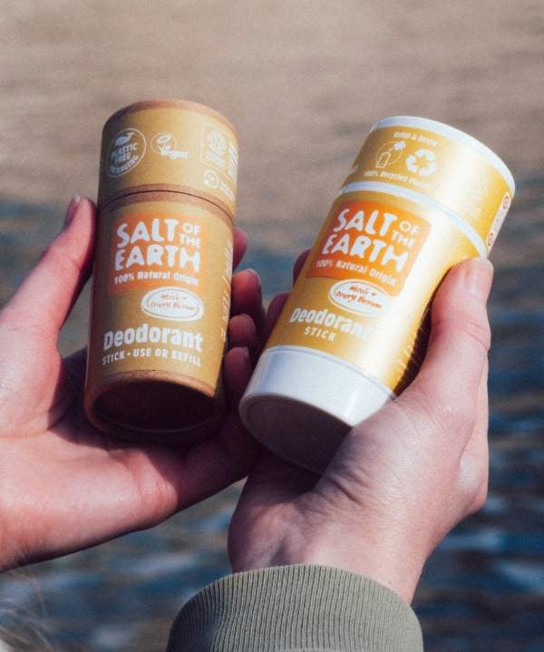 Hands holding Salt of the Earth Amber & Sandalwood deodorant sticks in recyclable and refillable packaging by the water