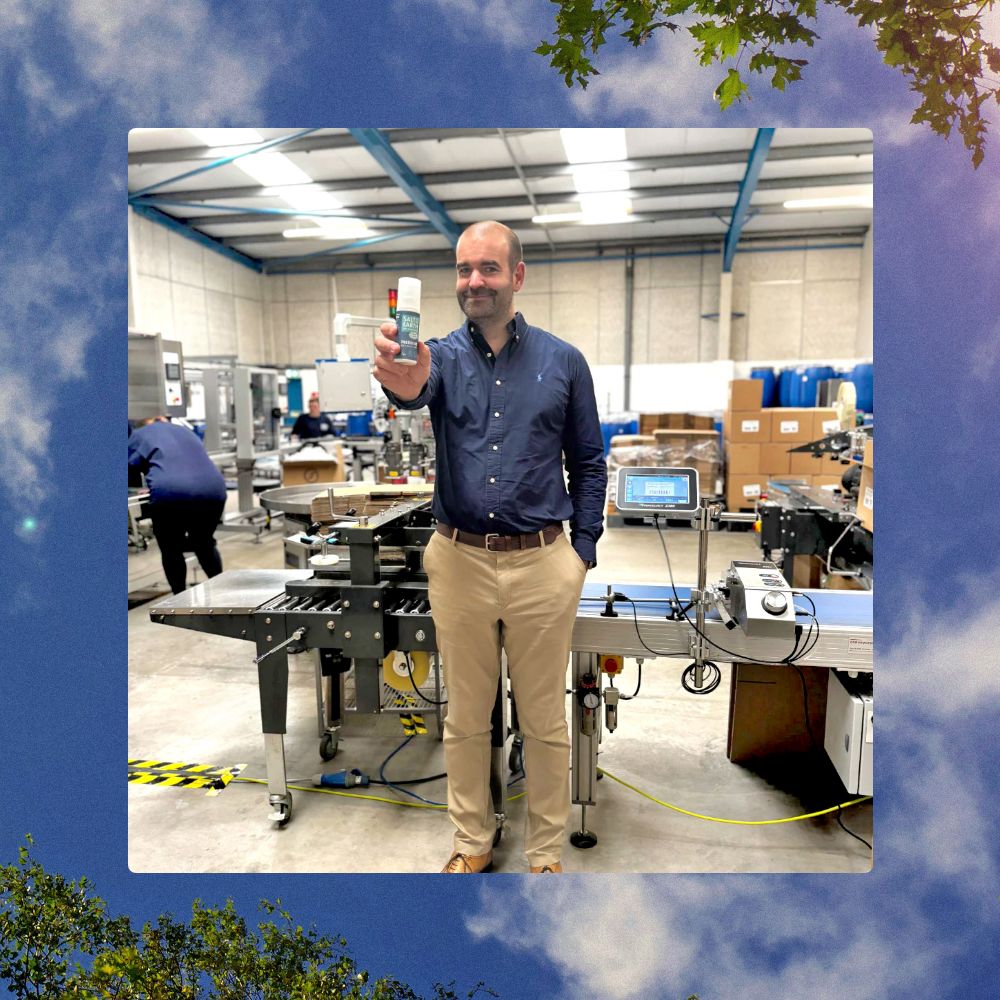 Thomas from Salt of the Earth holding a natural deodorant spray on the factory floor in front of the production line