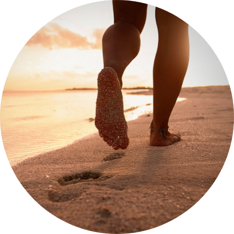 Person walking barefoot on a sandy UK beach at sunrise, symbolising a natural lifestyle journey with Salt of the Earth